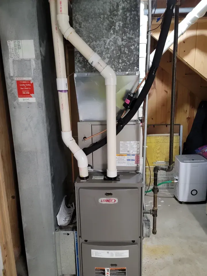 A furnace is sitting in a basement next to a pipe.