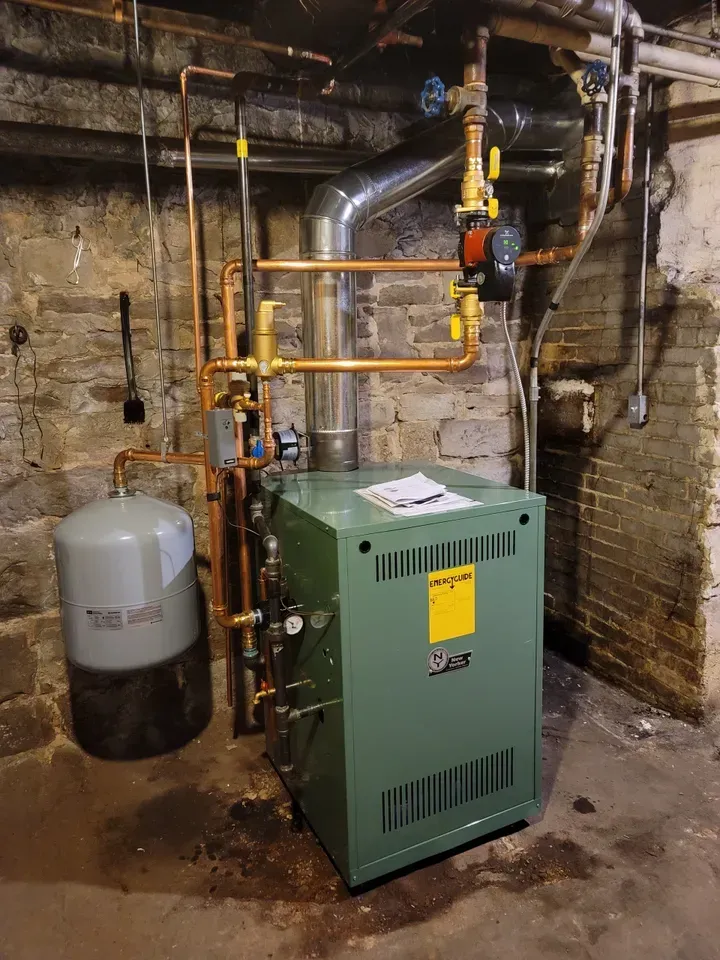 A green boiler is sitting in a basement next to a brick wall.
