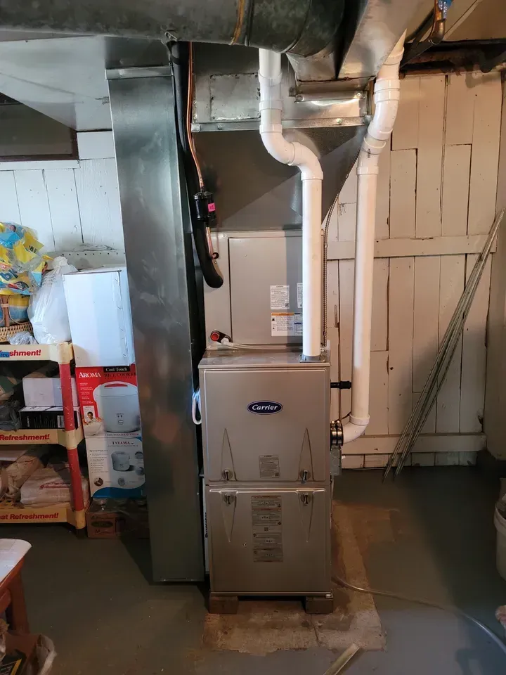 A stainless steel furnace is sitting in a basement next to a wooden fence.