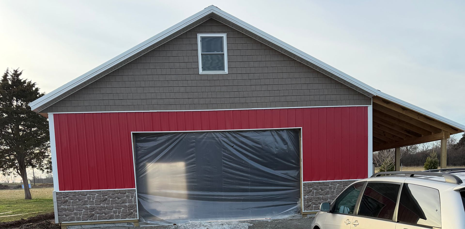 Construction of a wooden framed barn with a partially completed metal roof. Workers are installing walls.