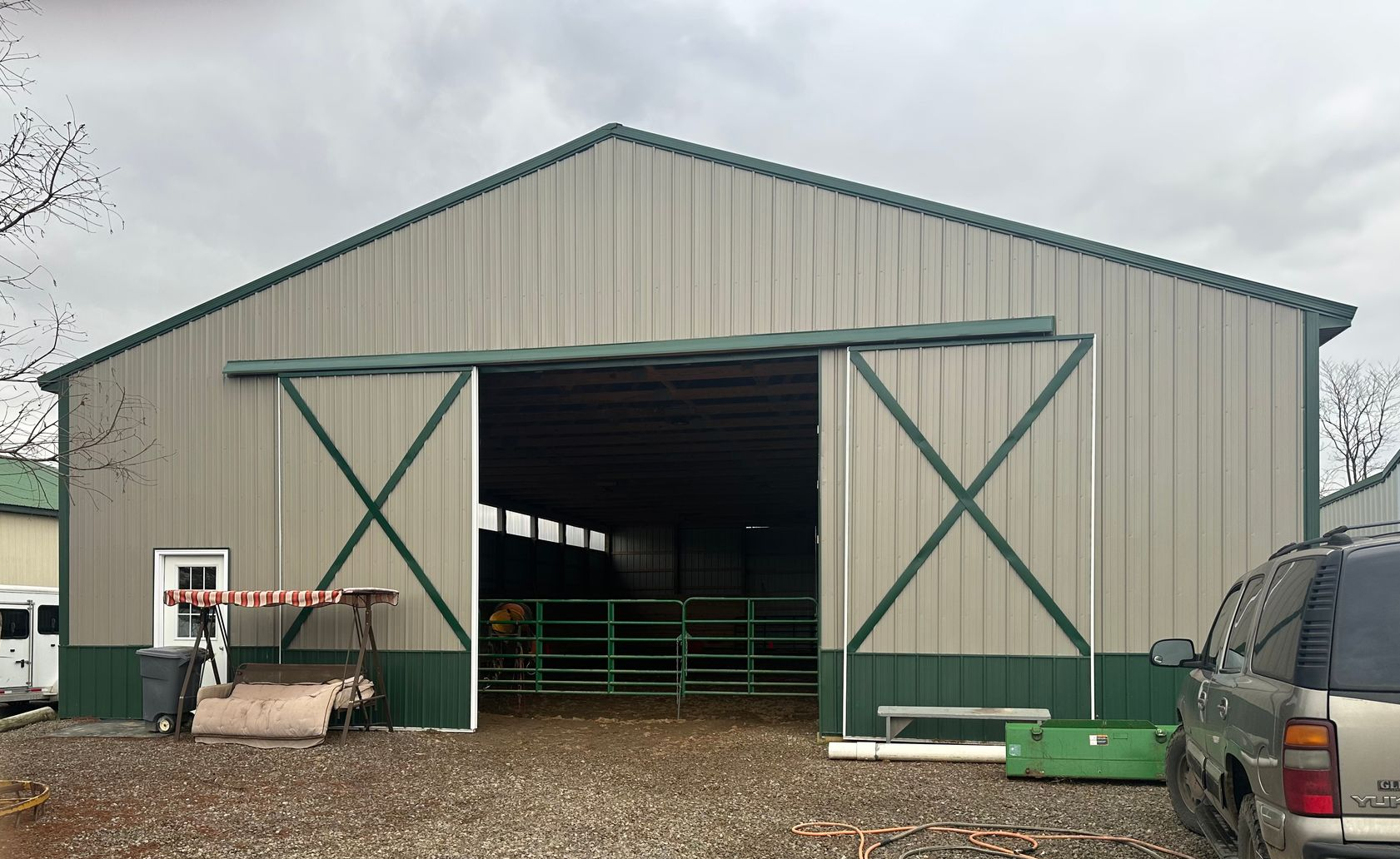 Large tan and green barn with open sliding doors, metal siding, and a gravel yard.