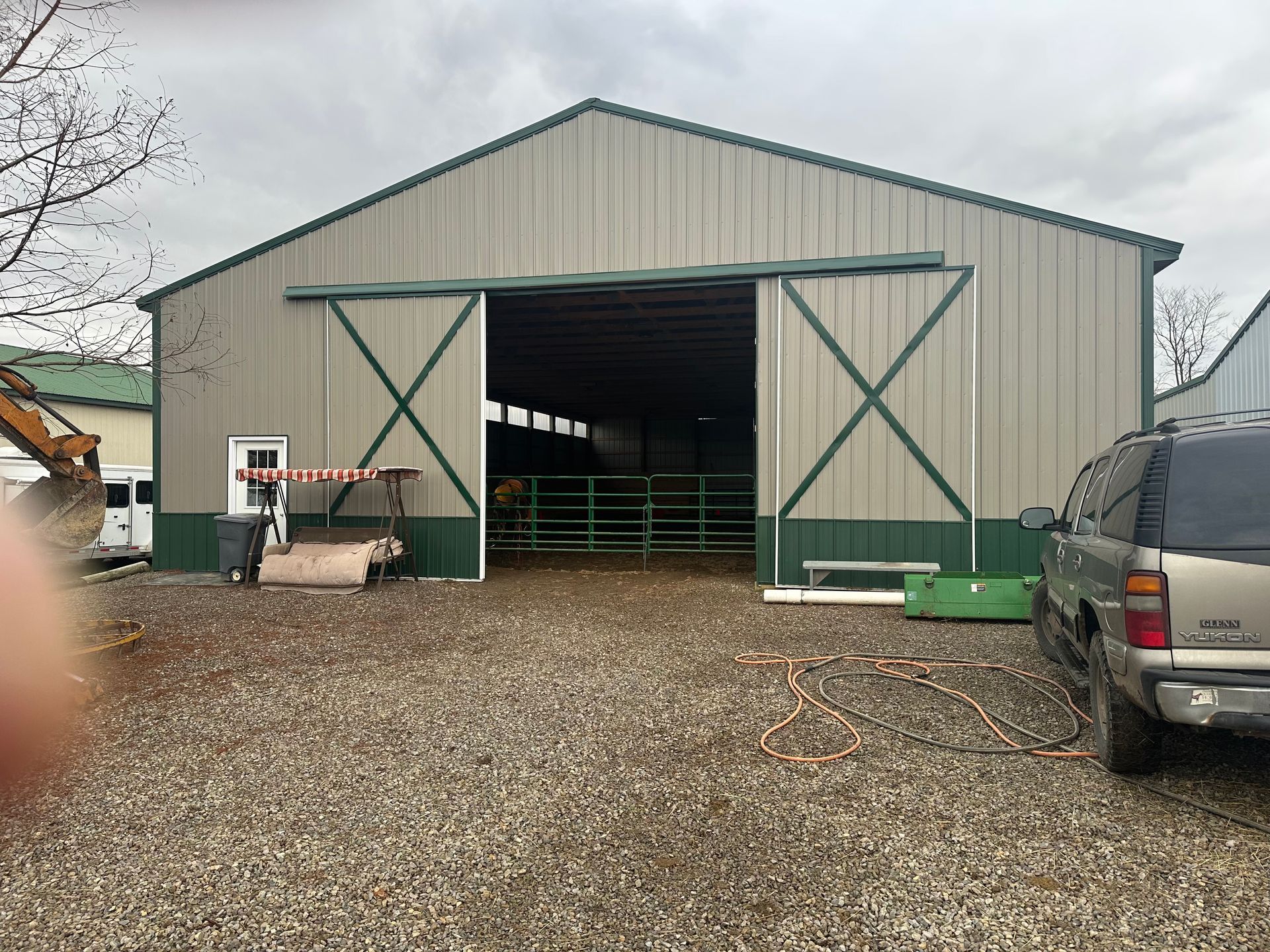 Large tan and green barn with open sliding doors, metal siding, and a gravel yard.