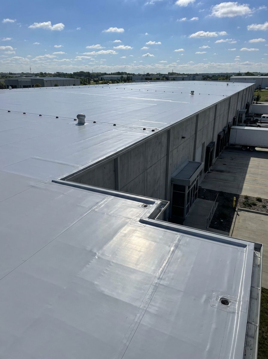 A flat white roof of a large commercial building under a partly cloudy blue sky.