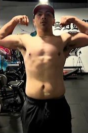 Man flexing arms in a gym. Wearing a cap and black sweatpants.