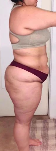 A person, side view, wearing a beige sports bra and burgundy underwear, standing indoors.