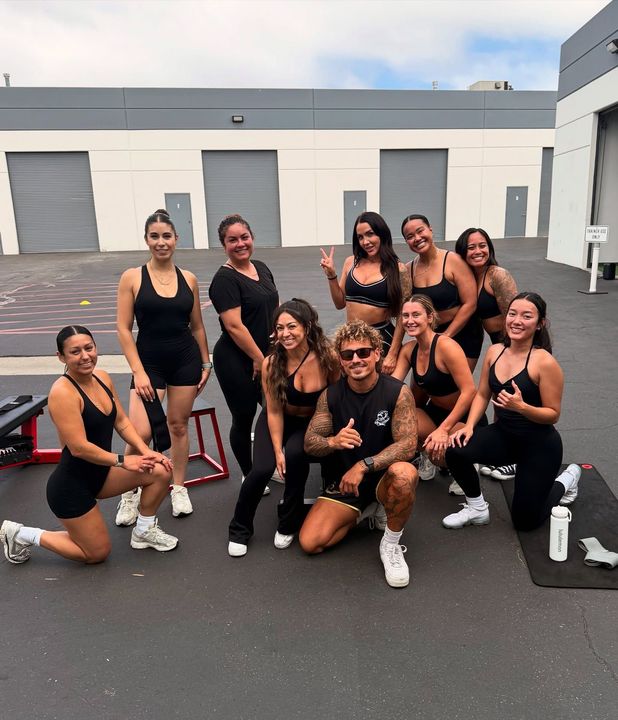 Group of people in workout clothes pose outside. Diverse group with smiles and athletic gear.