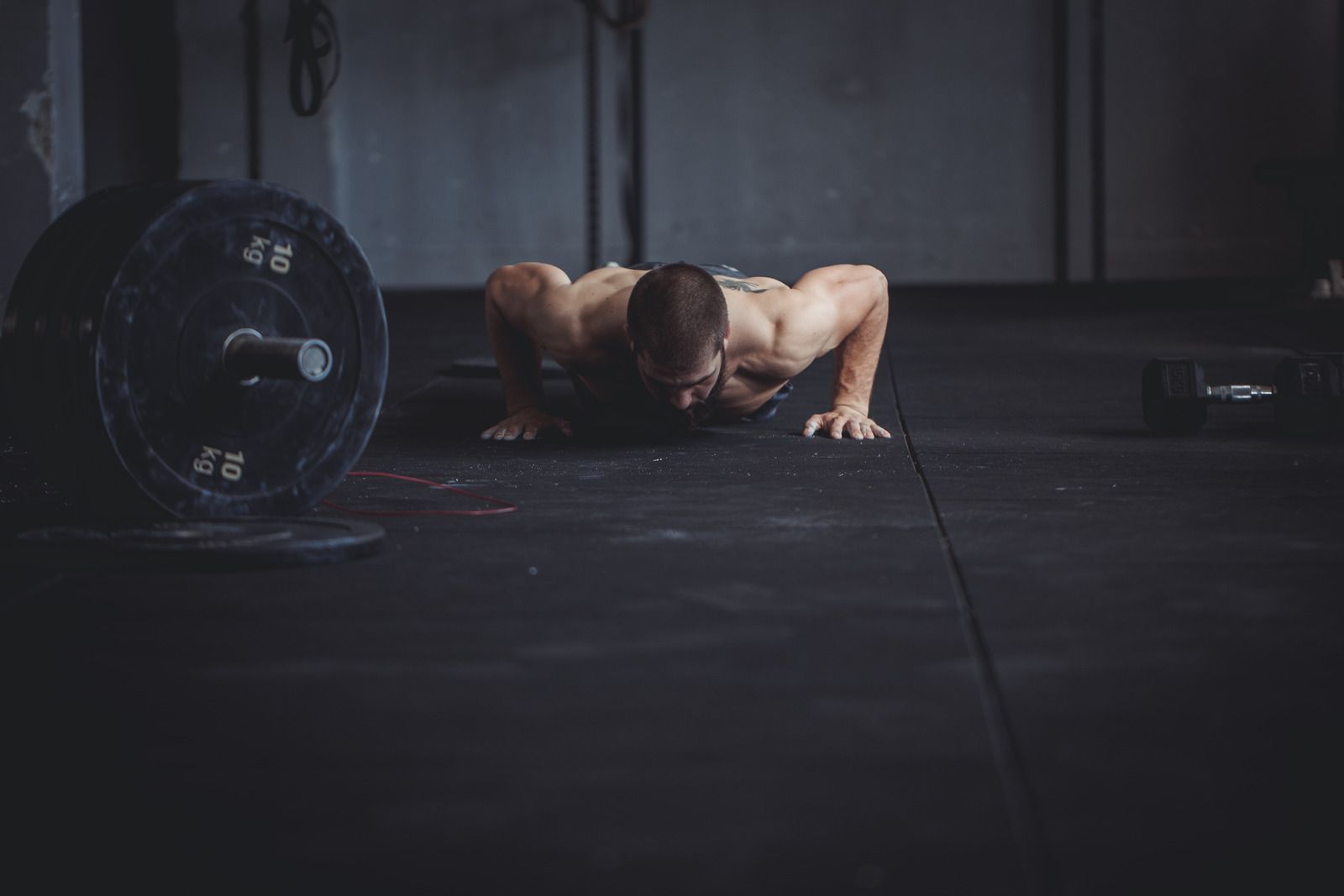 Man doing push-ups in a gym, next to a barbell on the floor.