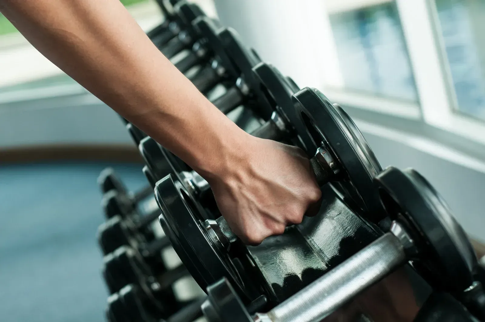 Hand selecting a dumbbell from a rack in a gym setting.
