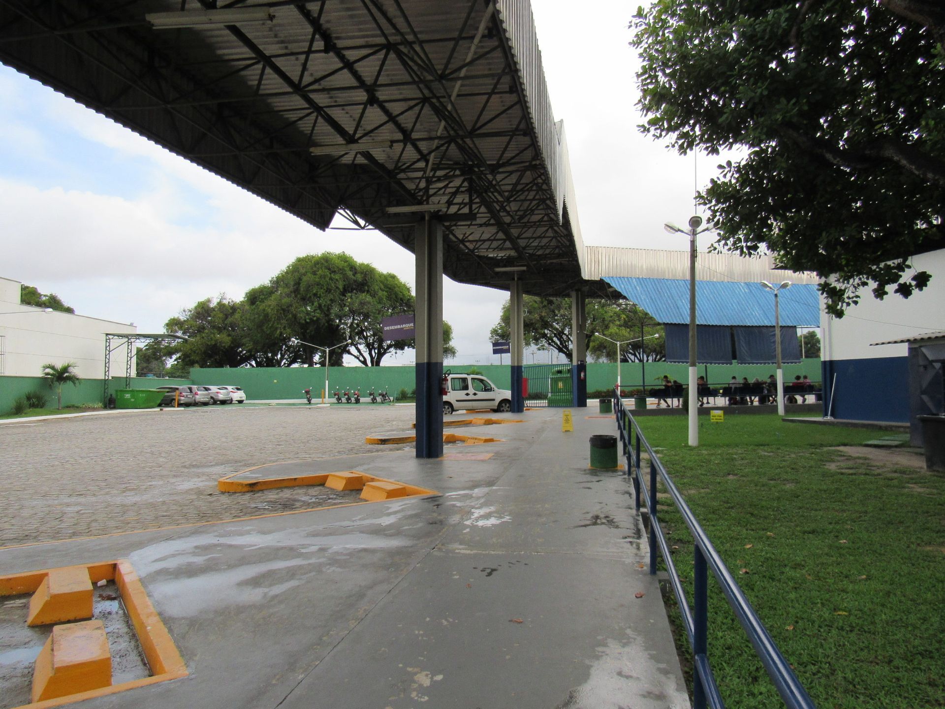 Estacionamento coberto com superfície de concreto e cascalho; van branca estacionada.