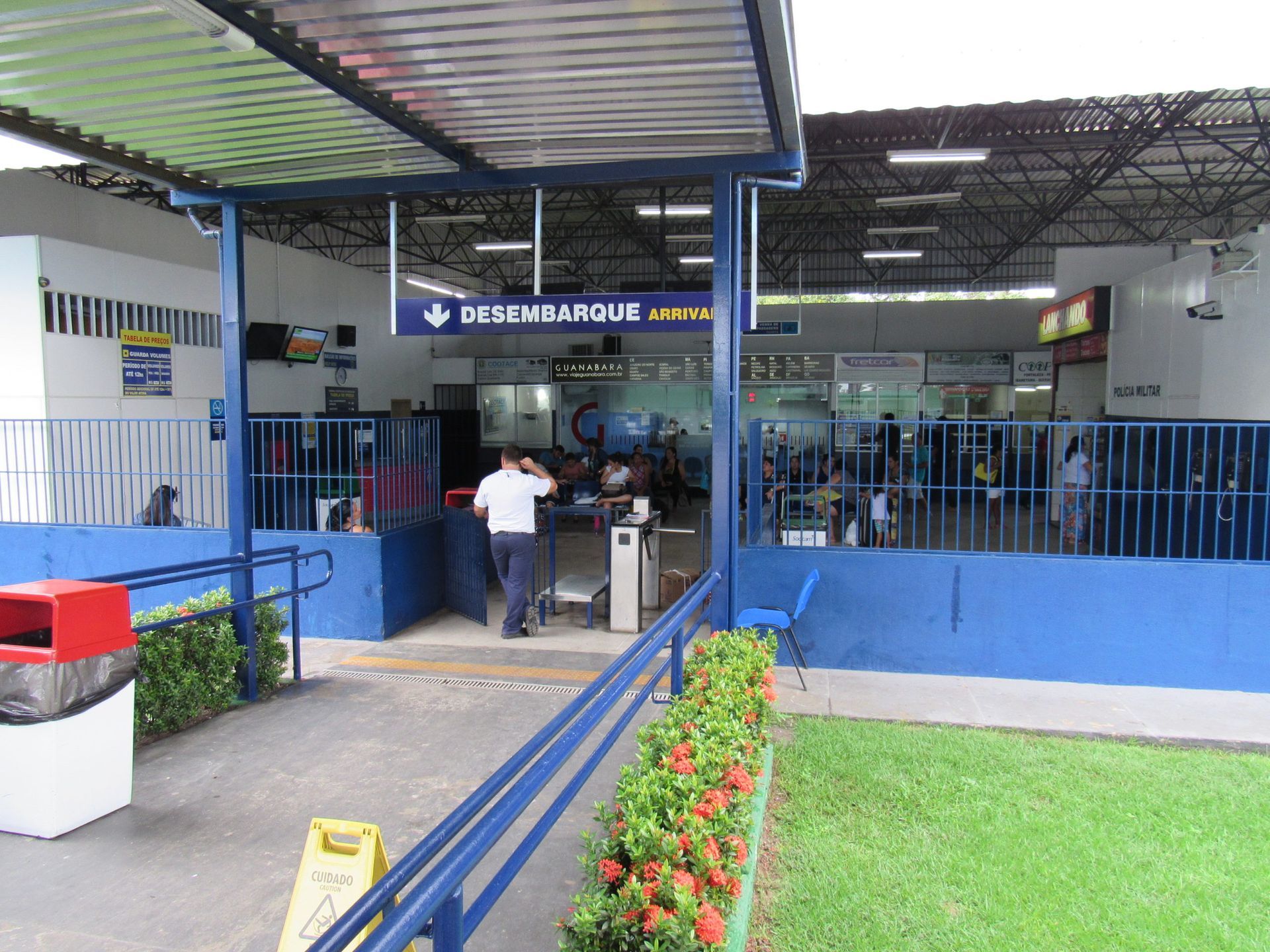 Homem na sala de controle falando ao telefone, supervisionando ônibus estacionados ao ar livre sob abrigo.