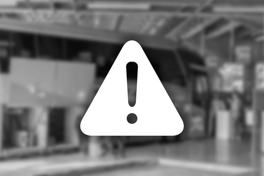 Triângulo de advertência branco com ponto de exclamação em frente a um fundo desfocado de uma garagem com um ônibus.