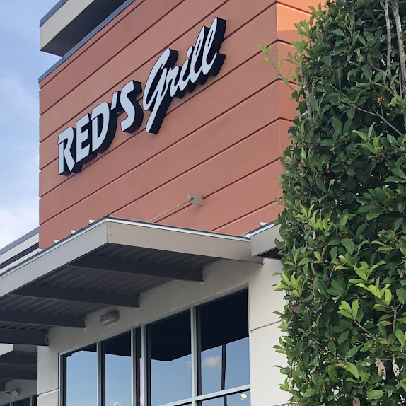 Red's Grill restaurant sign on a brown and white building with glass windows.