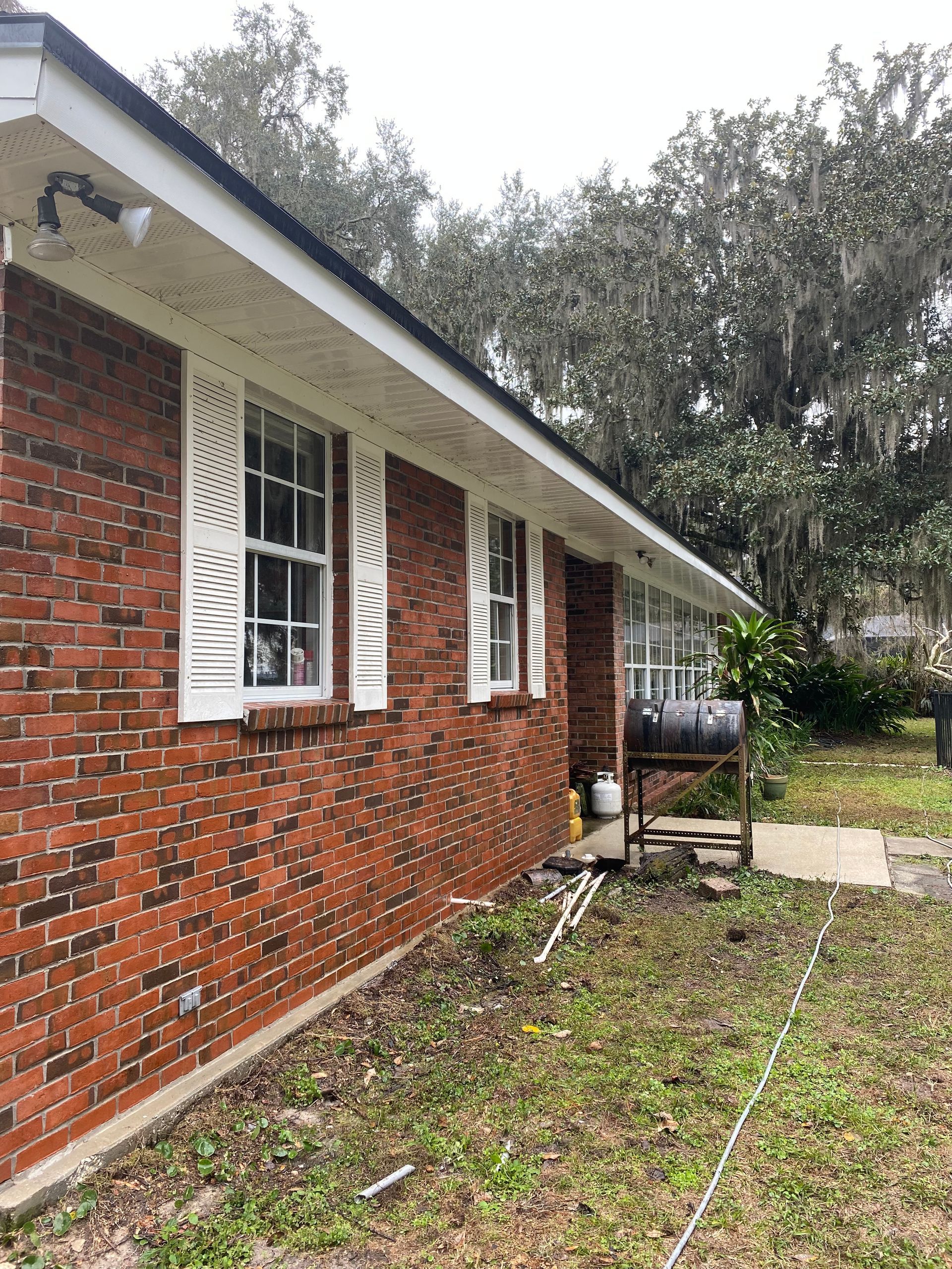 A brick house with white shutters and a barbecue grill in the backyard.