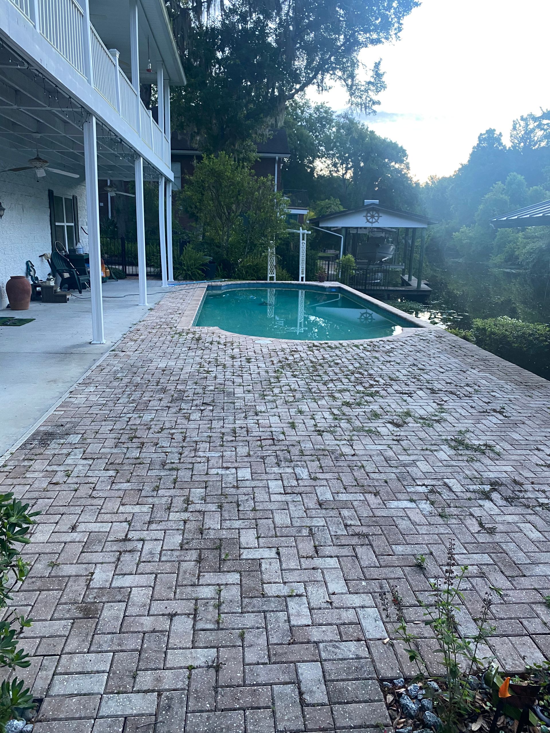 A large swimming pool is surrounded by a brick patio.