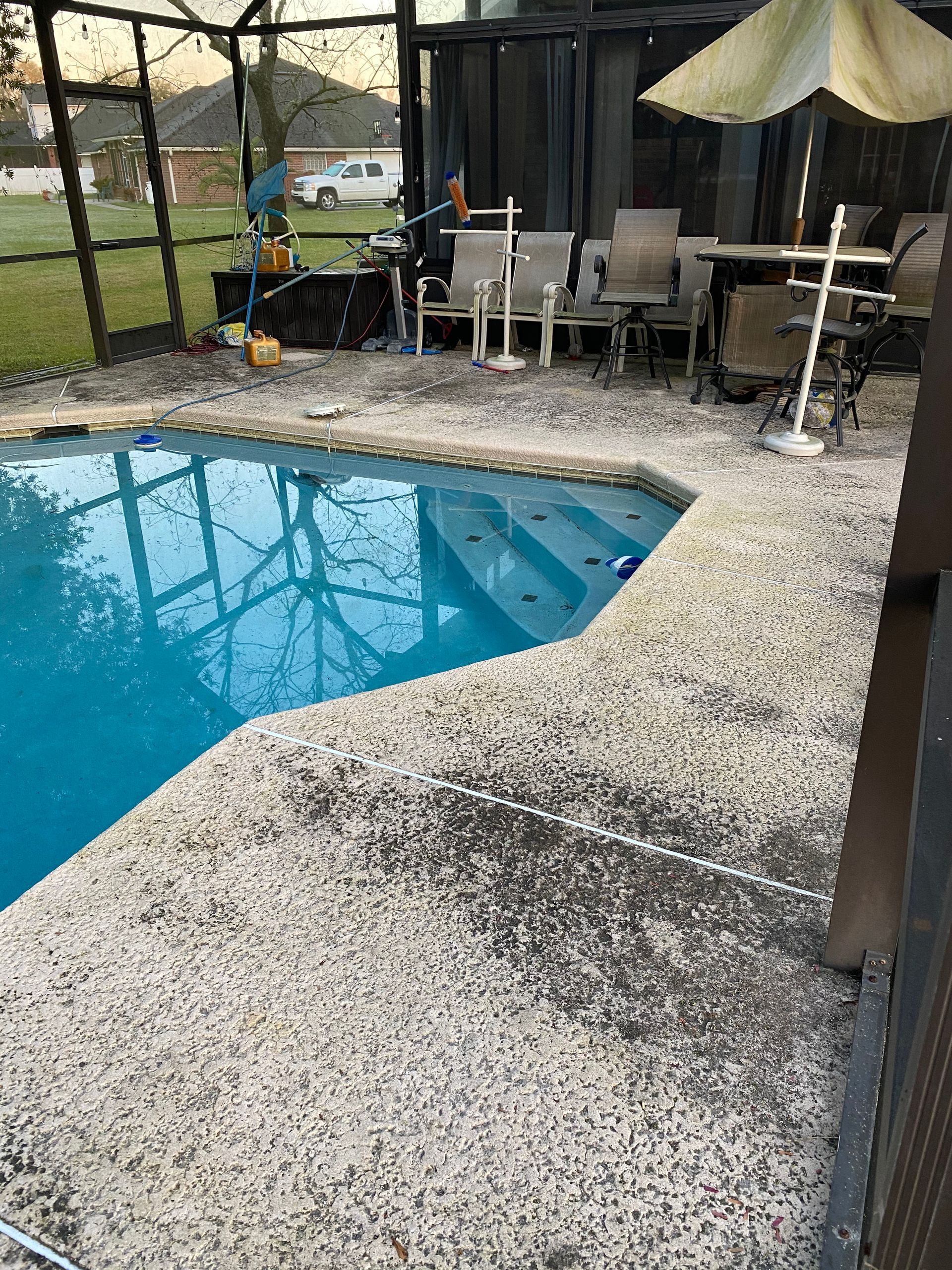 A swimming pool is surrounded by chairs and umbrellas in a backyard.