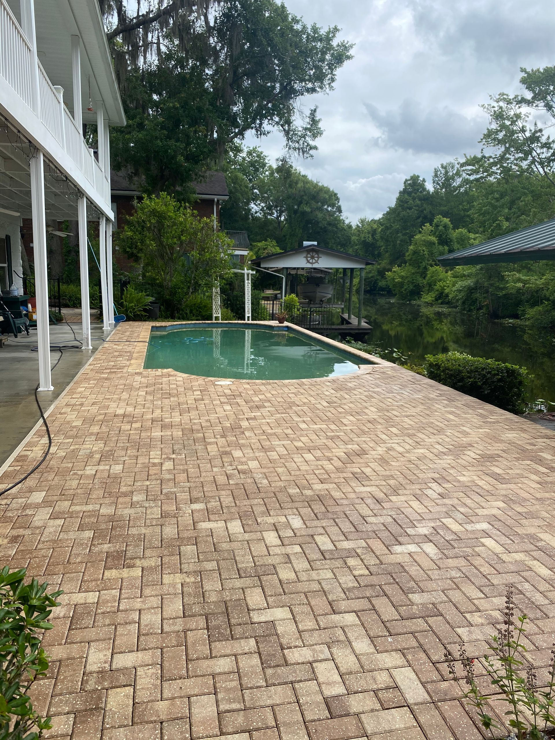 A large brick patio with a swimming pool in the background.