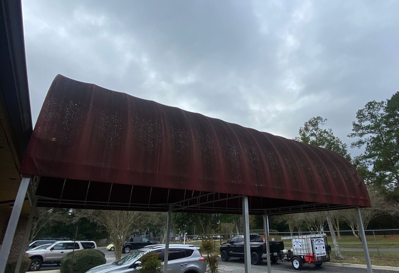 A carport with a red awning and cars parked underneath it.