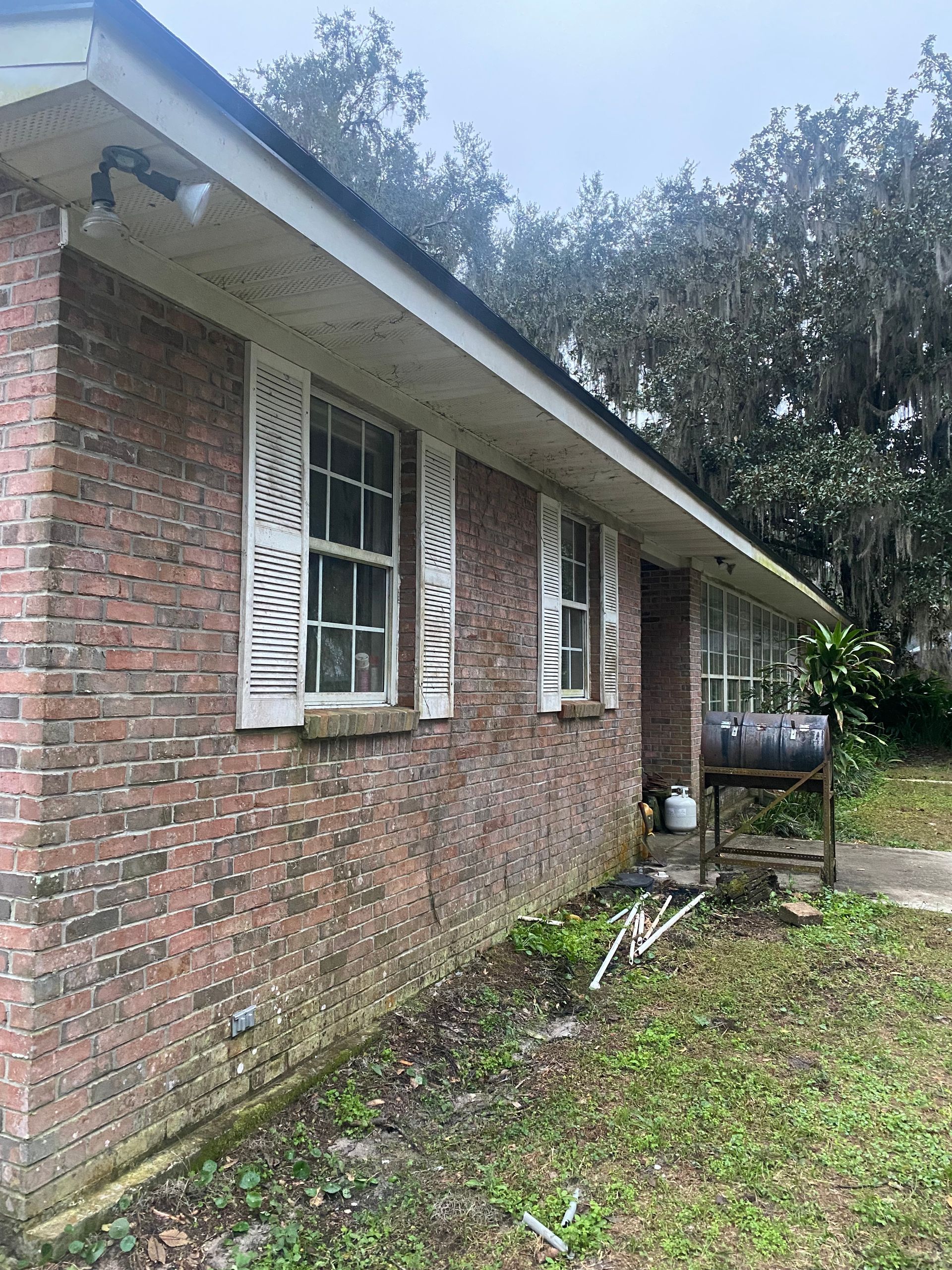 A brick house with white shutters and a barbecue grill in the backyard.