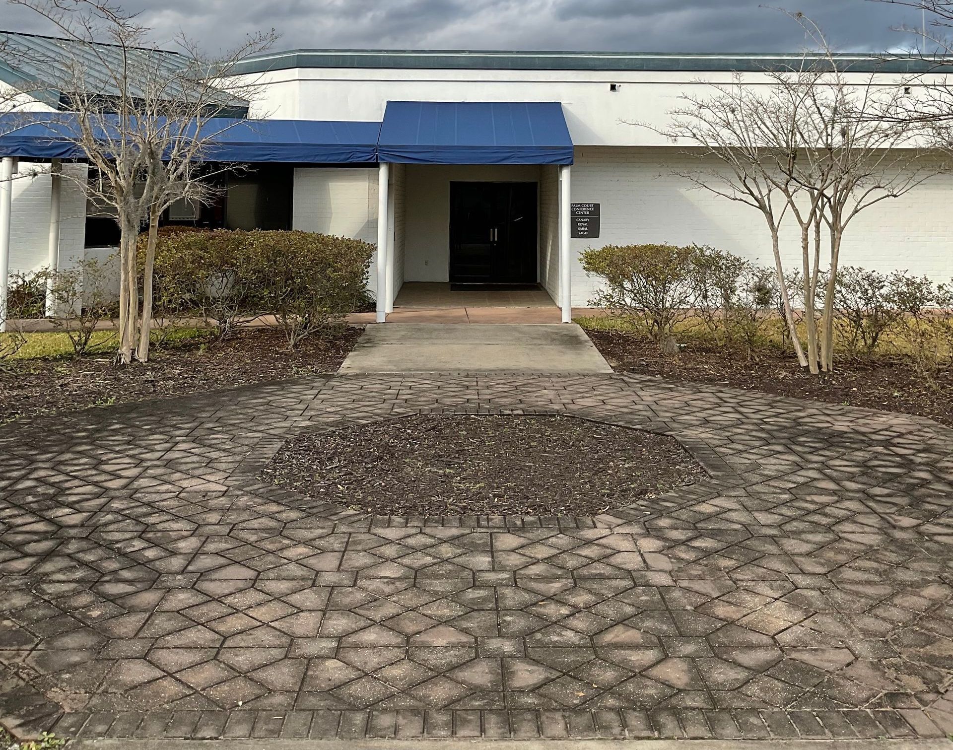 A white building with a blue awning and a brick walkway leading to it.