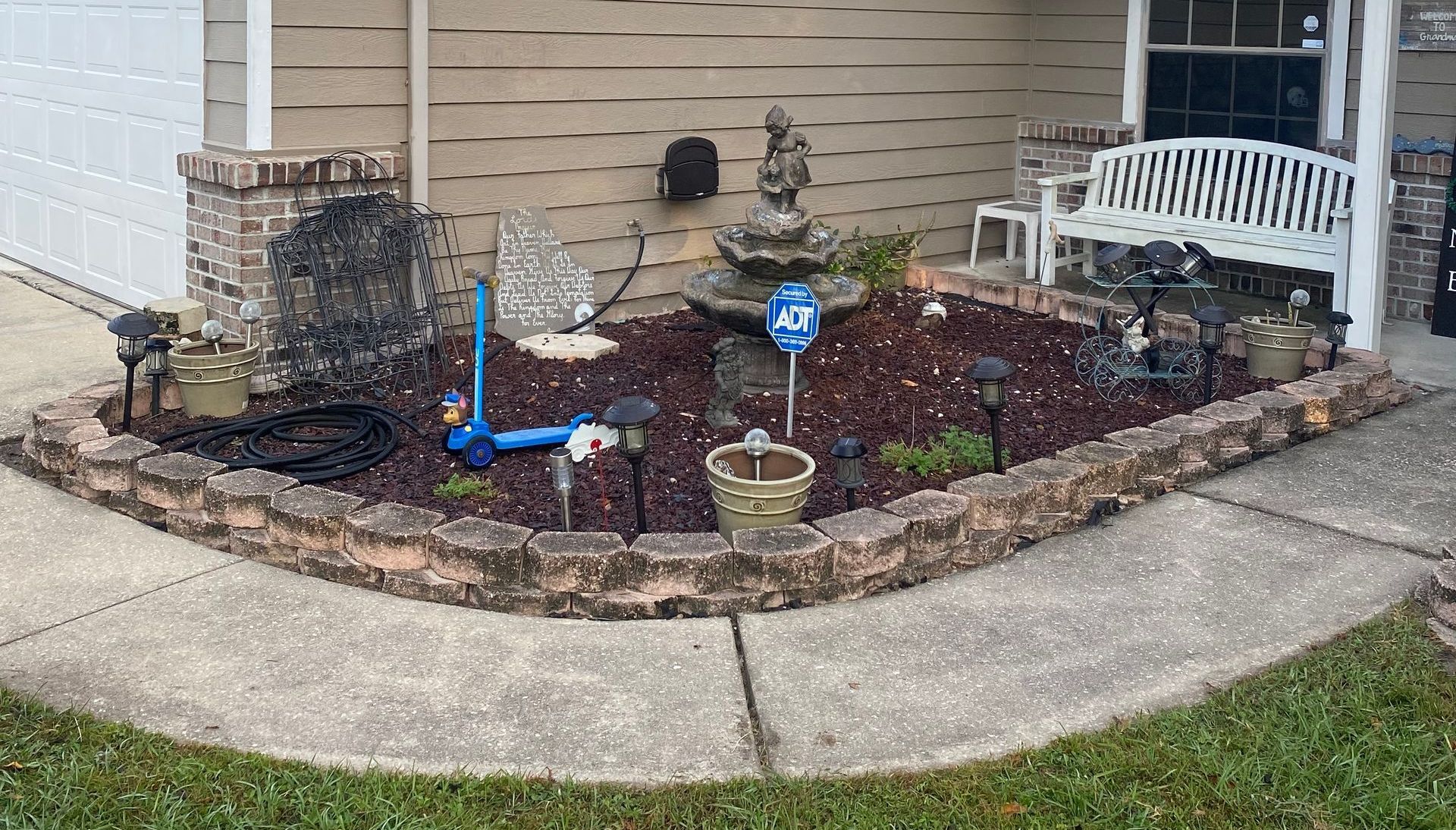 A garden with a fountain and a bench in front of a house.