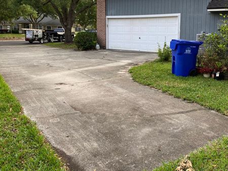 A blue trash can is sitting on the side of a driveway next to a garage door.