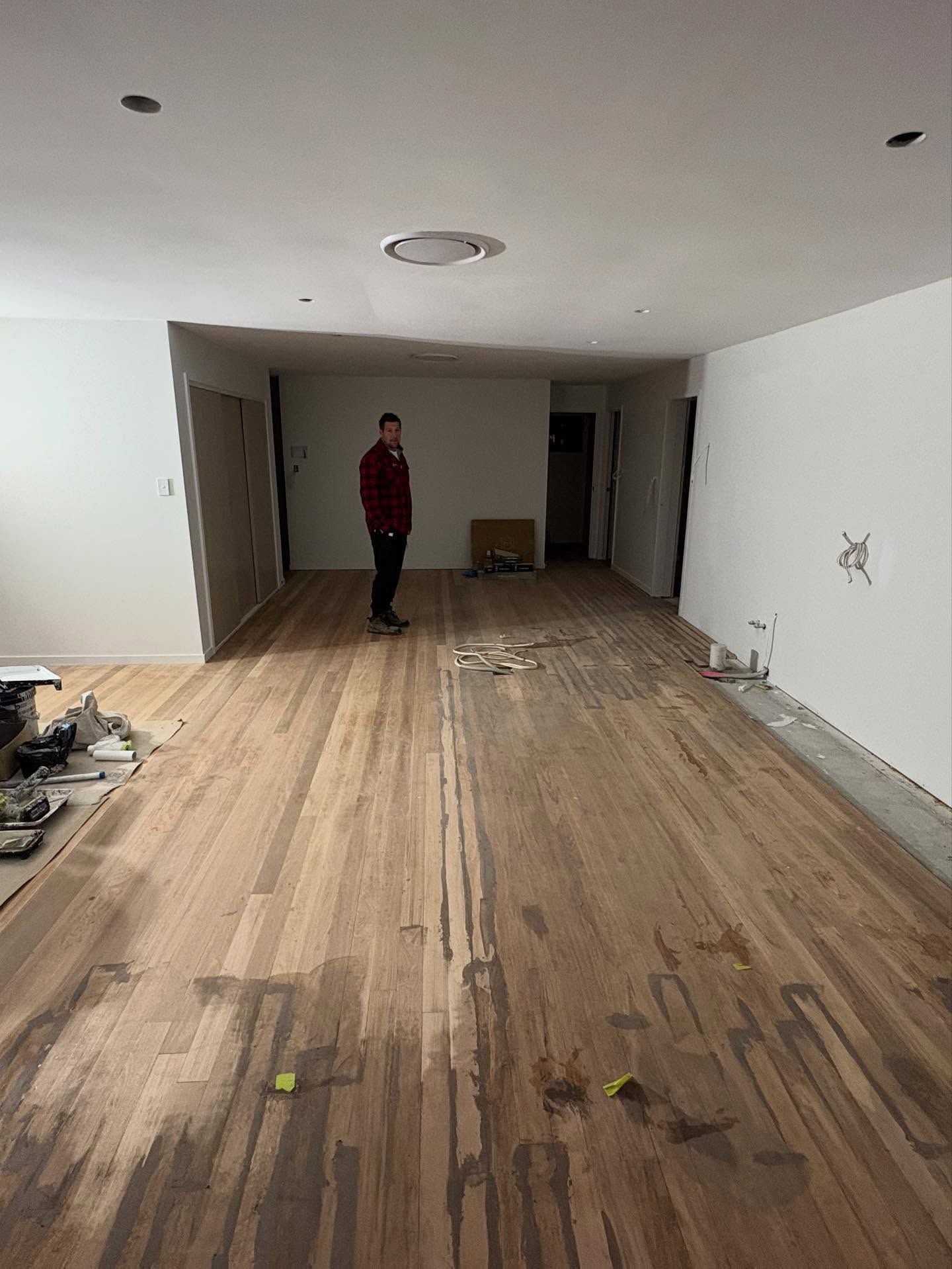 Empty room with wood floor, white walls, and a person standing near the back wall.