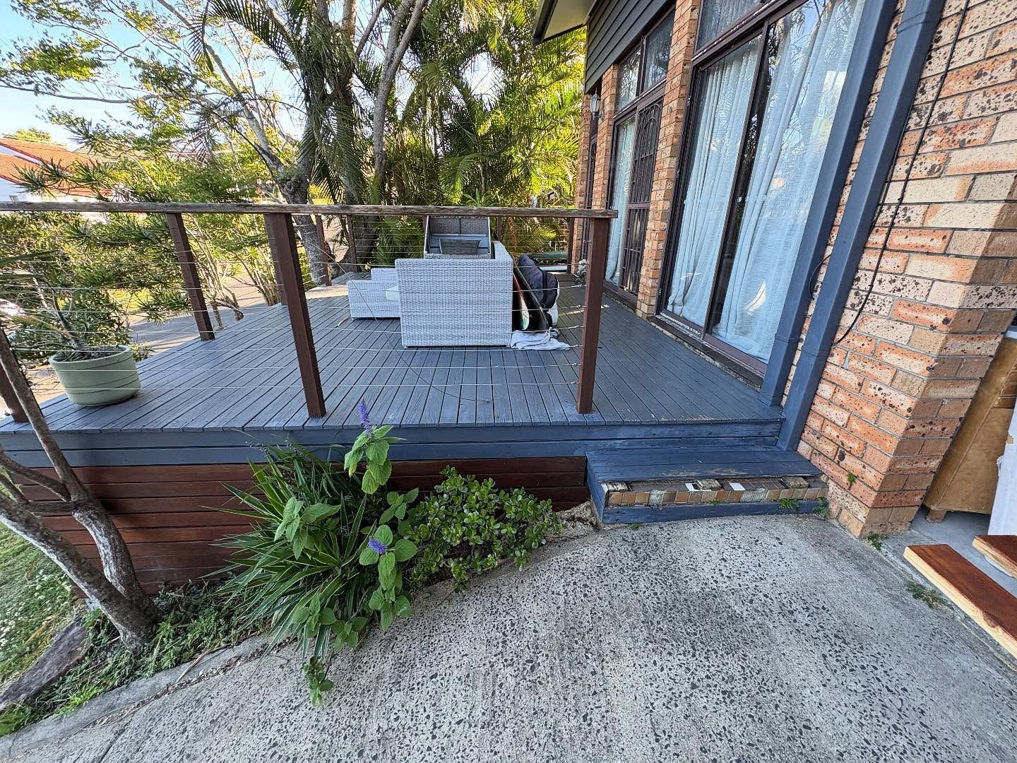 Balcony patio with metal railing, gray table and chairs, brick wall, and potted plants overlooking trees