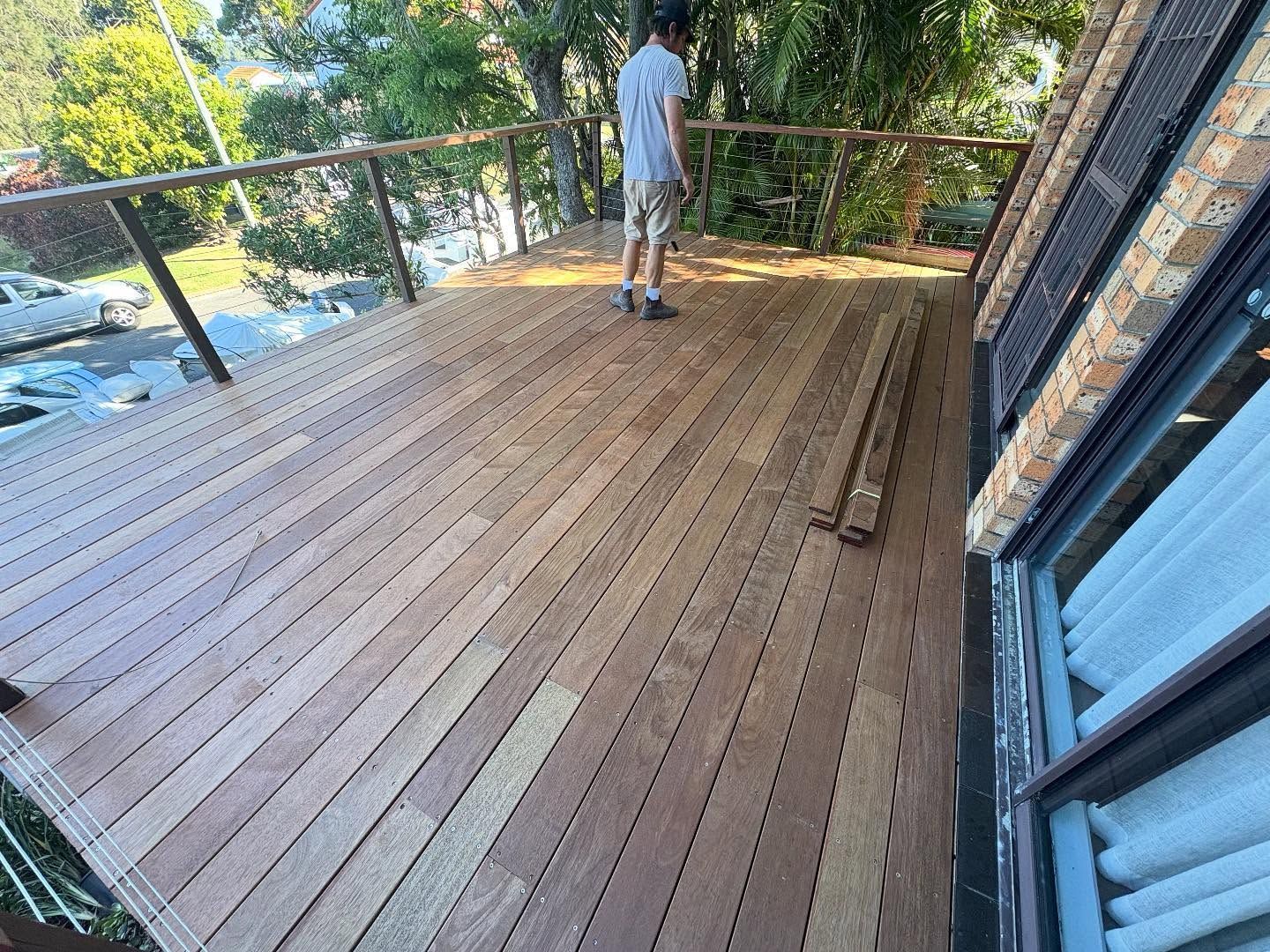 Wooden deck overlooking water, with a person standing near the railing and a sliding glass door on the right.