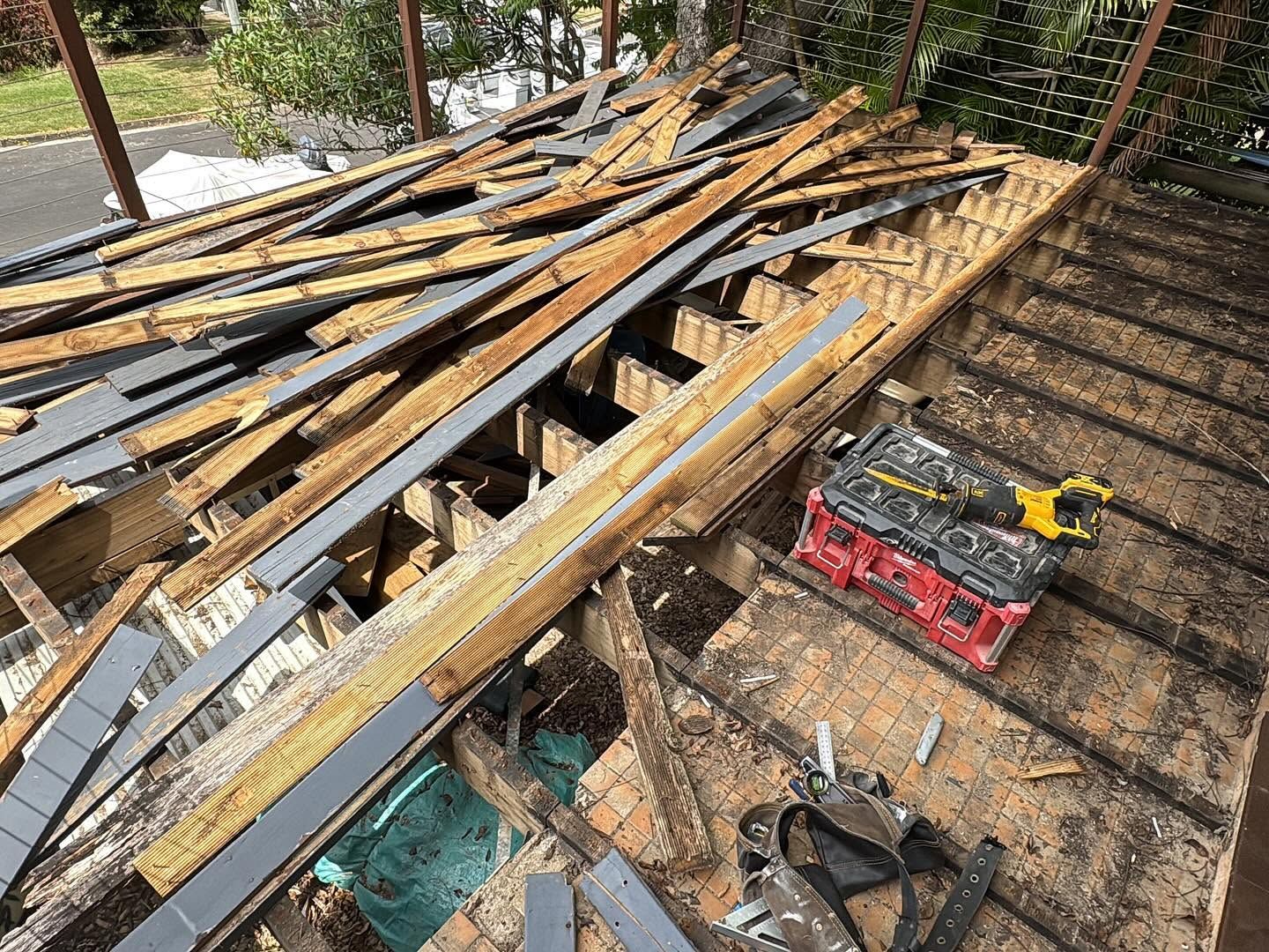 Pile of wooden boards and metal scraps on a deck beside a red toolbox and fence.