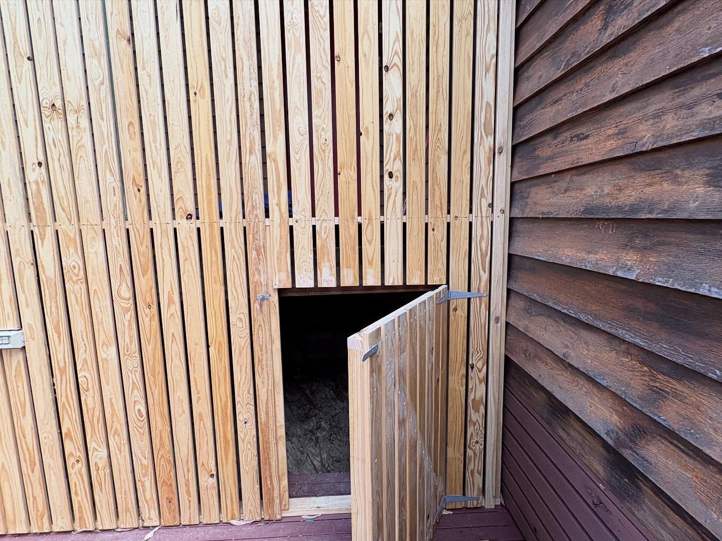 Wooden building exterior with a small open doorway and vertical slatted walls.