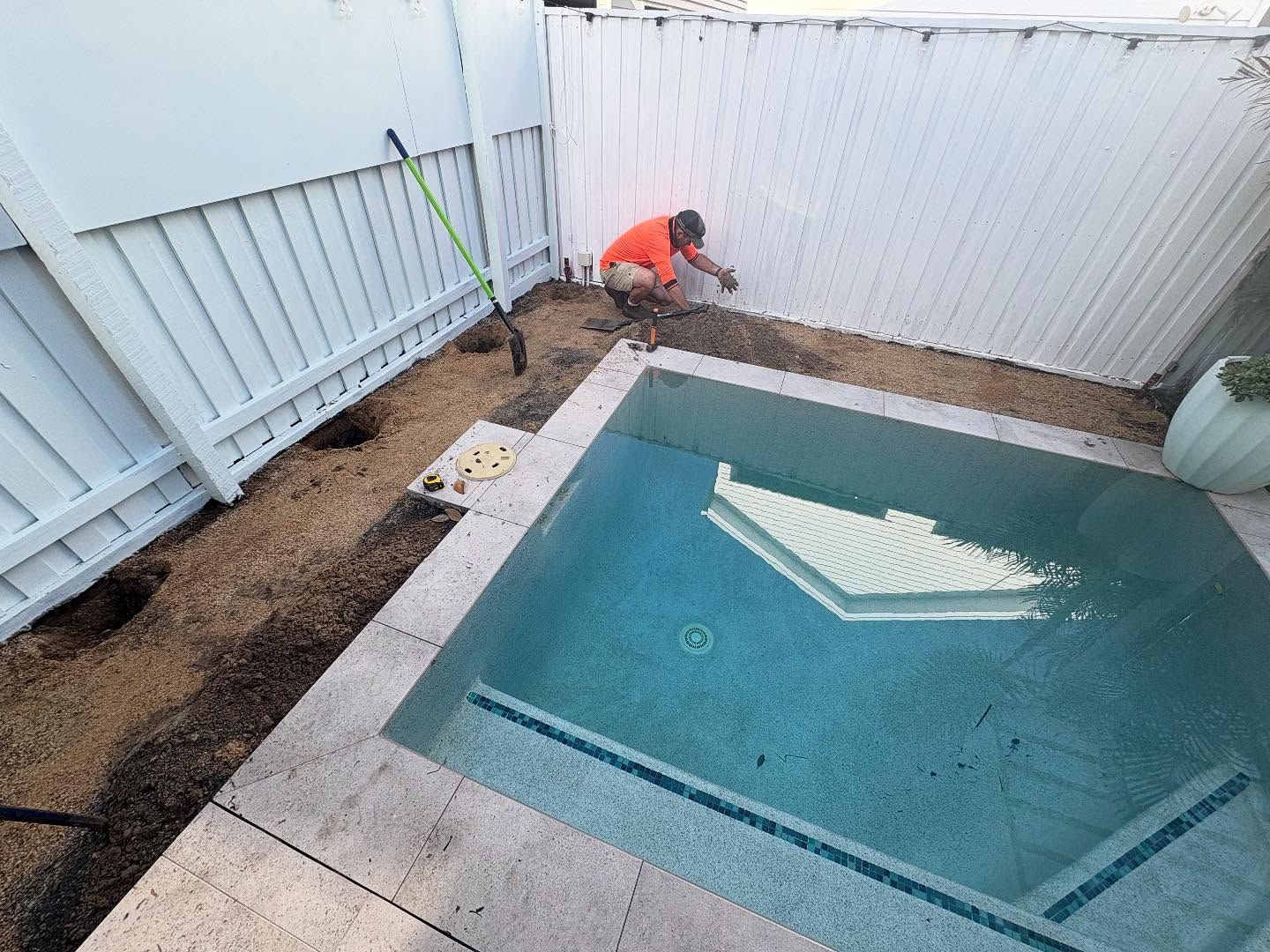 Backyard pool with a worker in an orange shirt cleaning along the fence