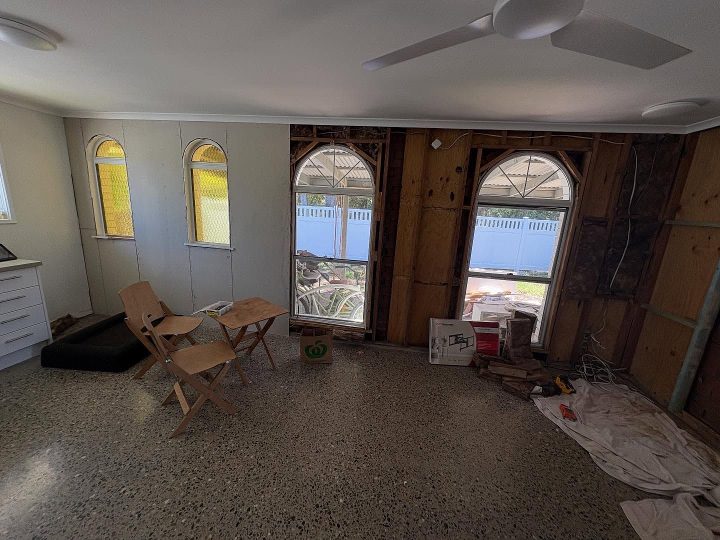 Empty room with large arched windows overlooking water, ceiling fan, and folded chairs on the floor