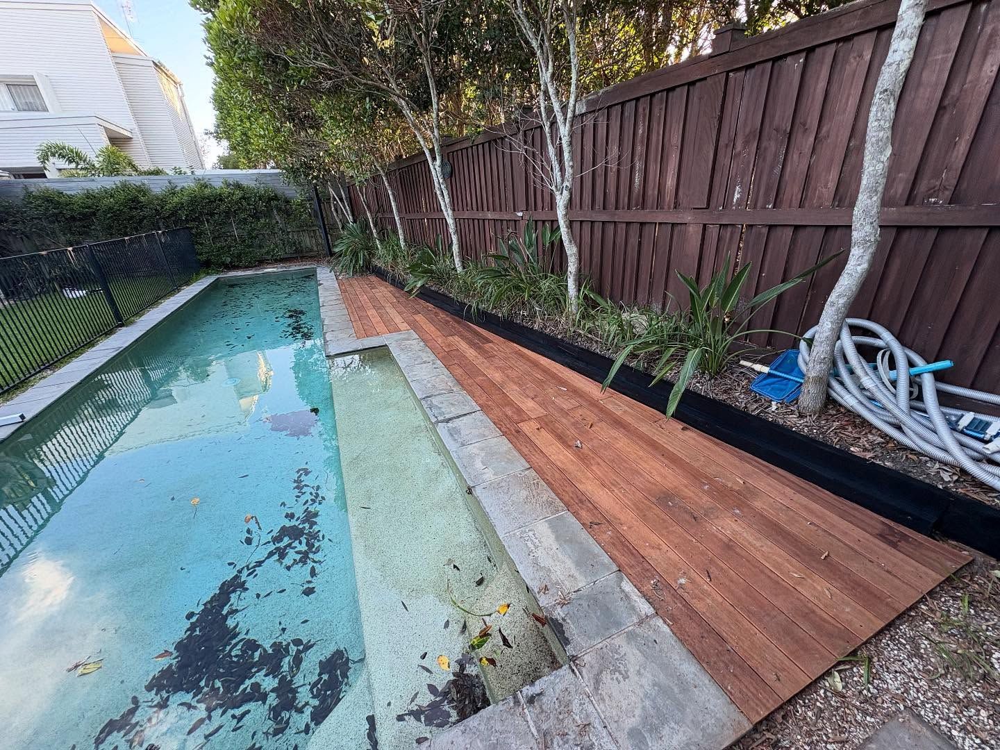 Backyard pool with a wooden deck, fence, and a partially covered, empty pool.