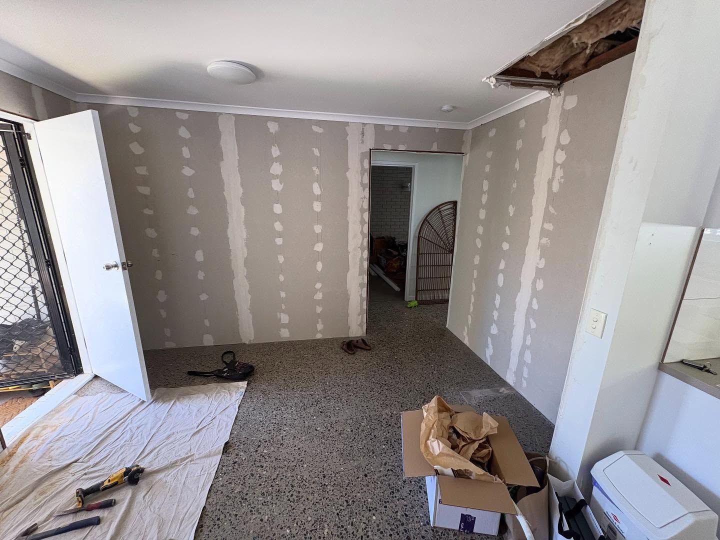 Damaged room under renovation with exposed drywall, debris on the floor, and a hole in the ceiling
