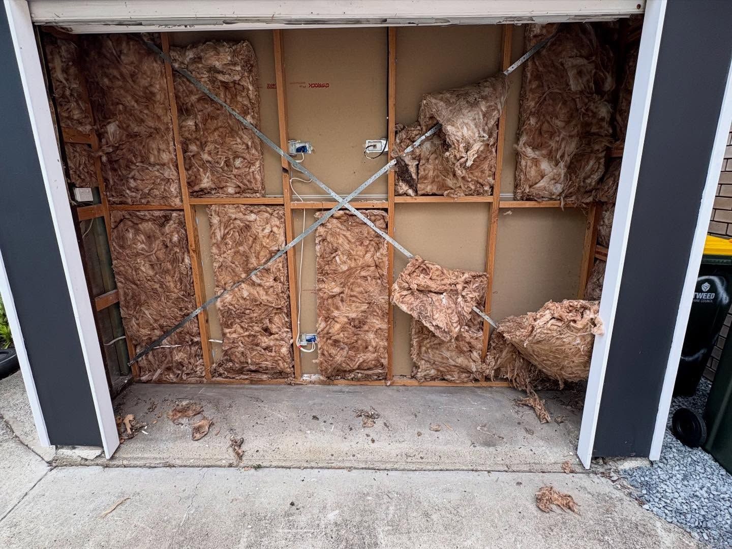 Partially boarded garage opening with exposed insulation and cross-braced plywood doorpanel