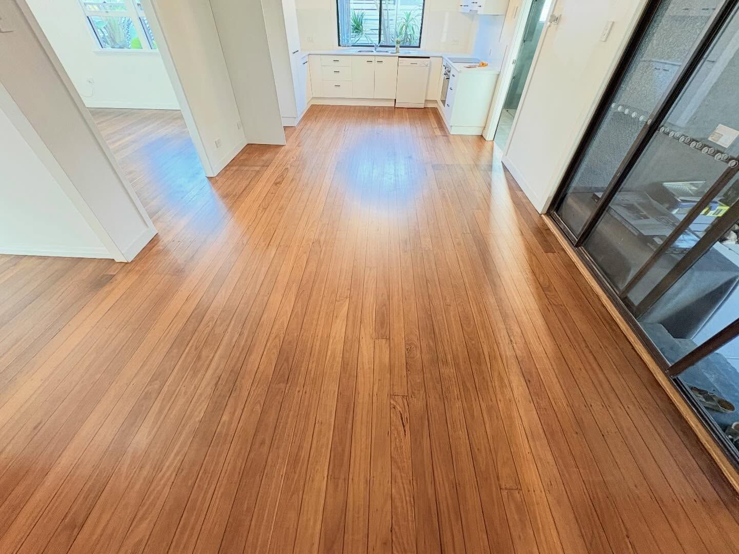 Empty room with wood floors, white walls, windows, and a glass sliding door.