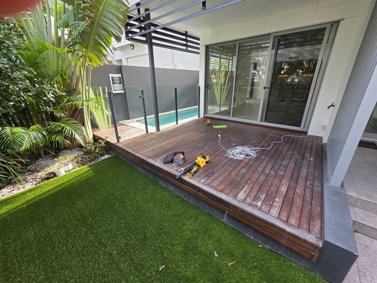 Small backyard patio with wooden deck, green turf, glass sliding doors, and tools on the floor