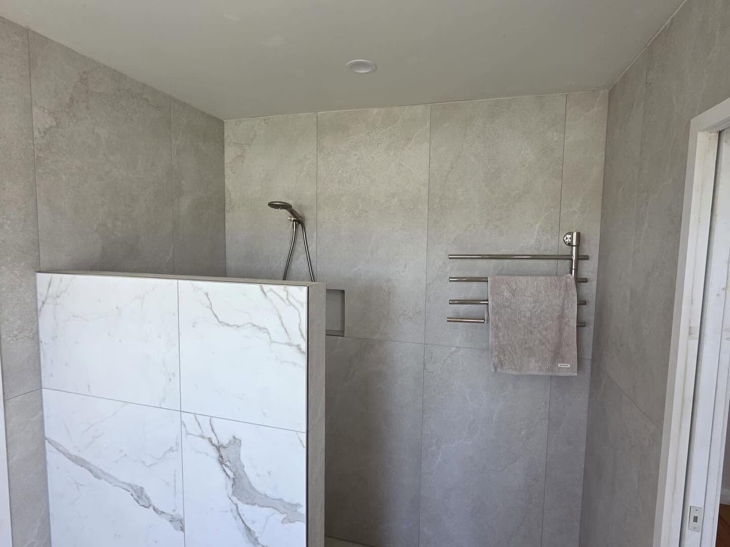Modern bathroom with unfinished gray walls, white marble shower panel, and towel rack.