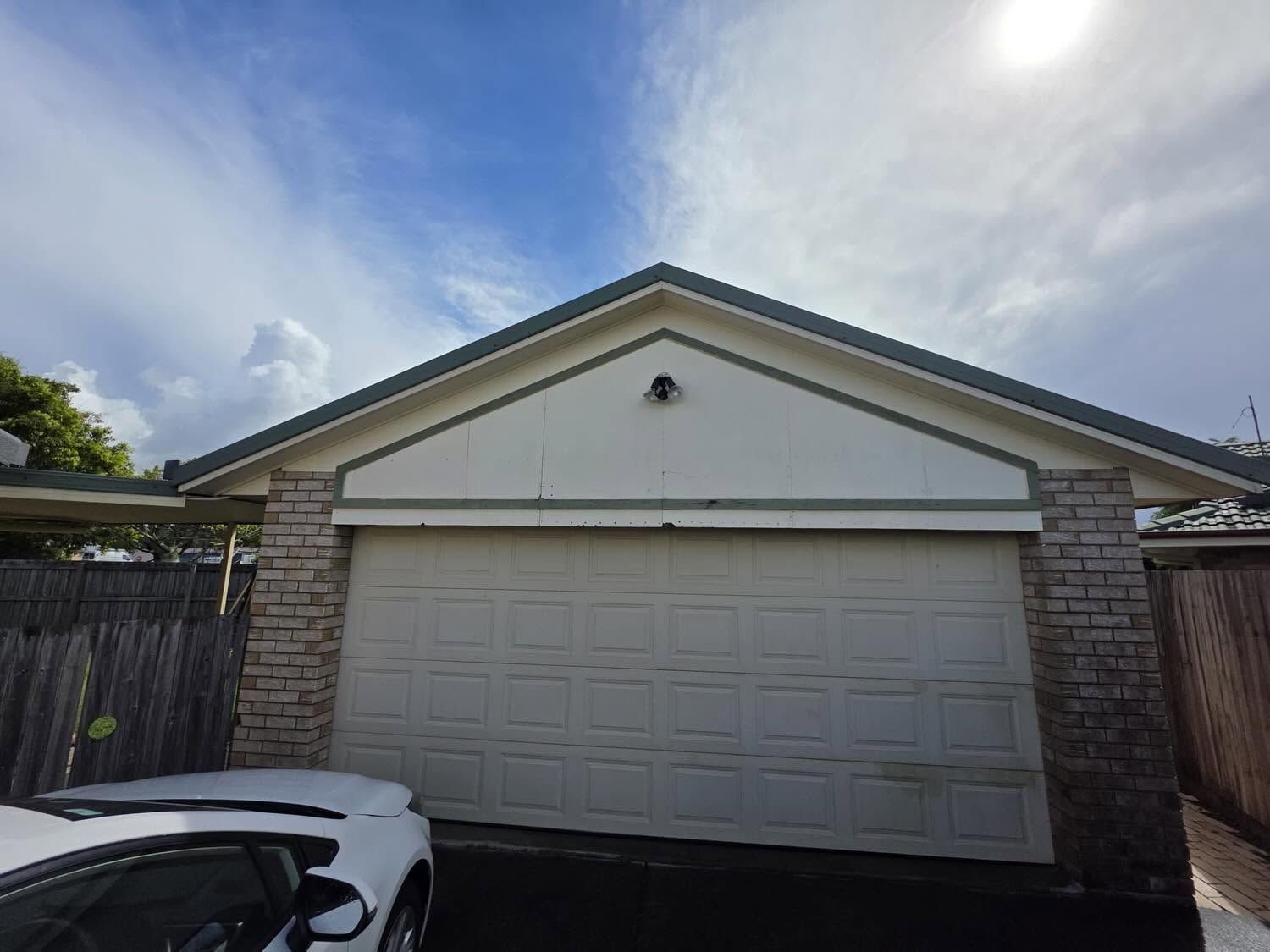 White double garage door on a brick house under a blue sky, with a car partially visible at left.