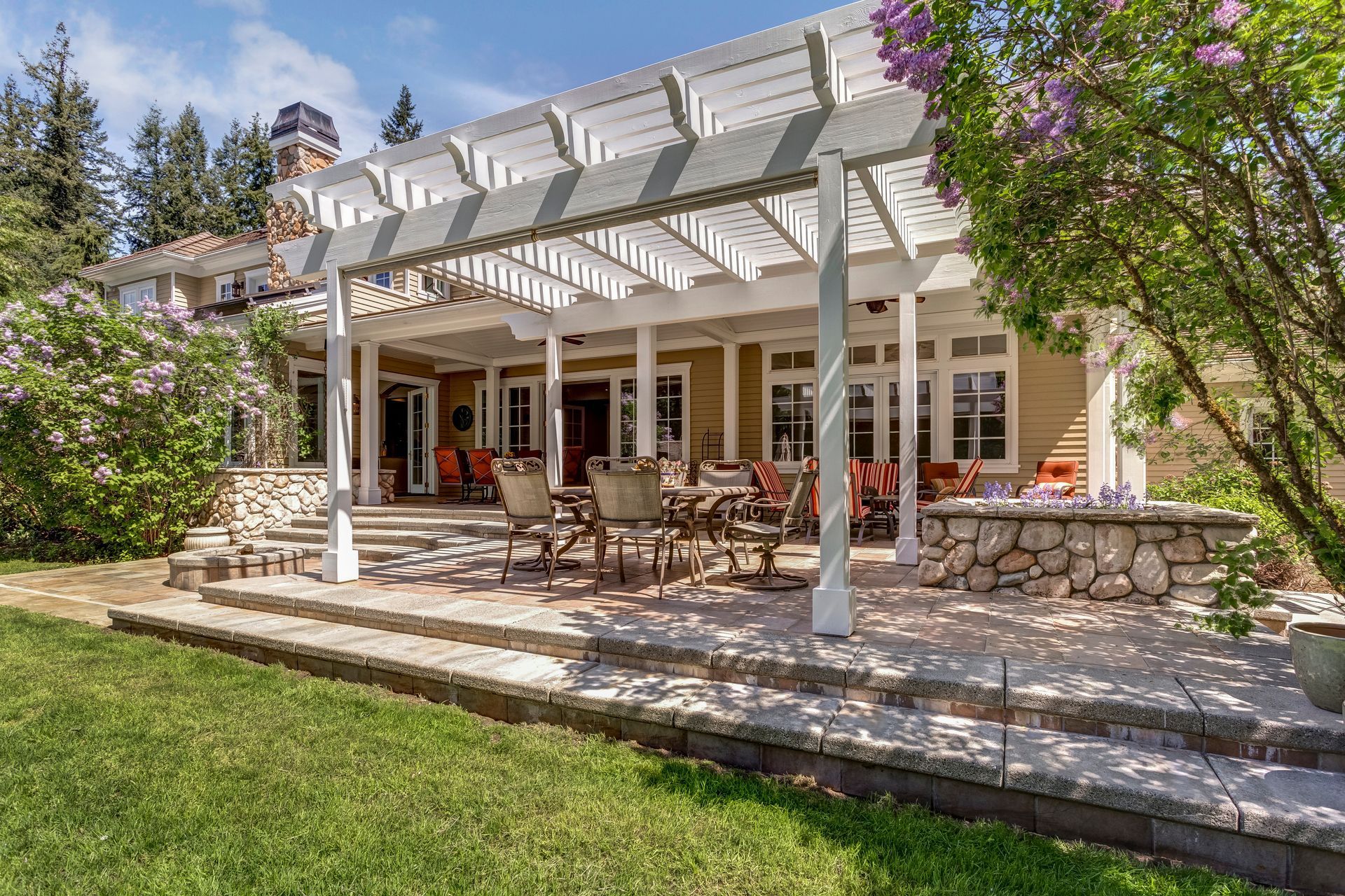 Stone patio with white pergola and outdoor dining set beside a house and green lawn