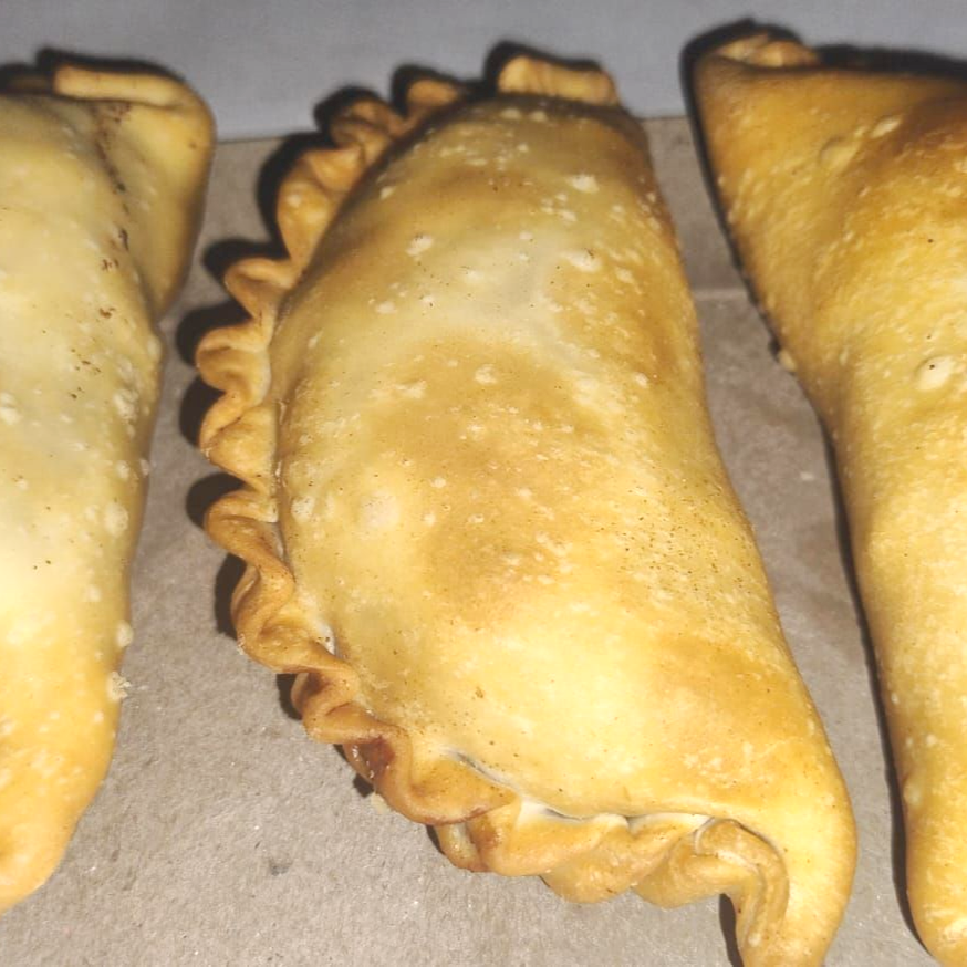 Tres empanadas doradas sobre papel marrón, una sabrosa masa rellena de carne y verduras.