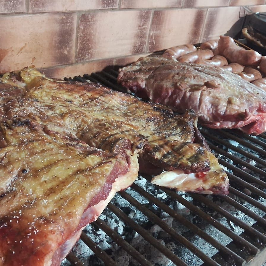 Grandes trozos de carne y embutidos asados sobre brasas calientes.