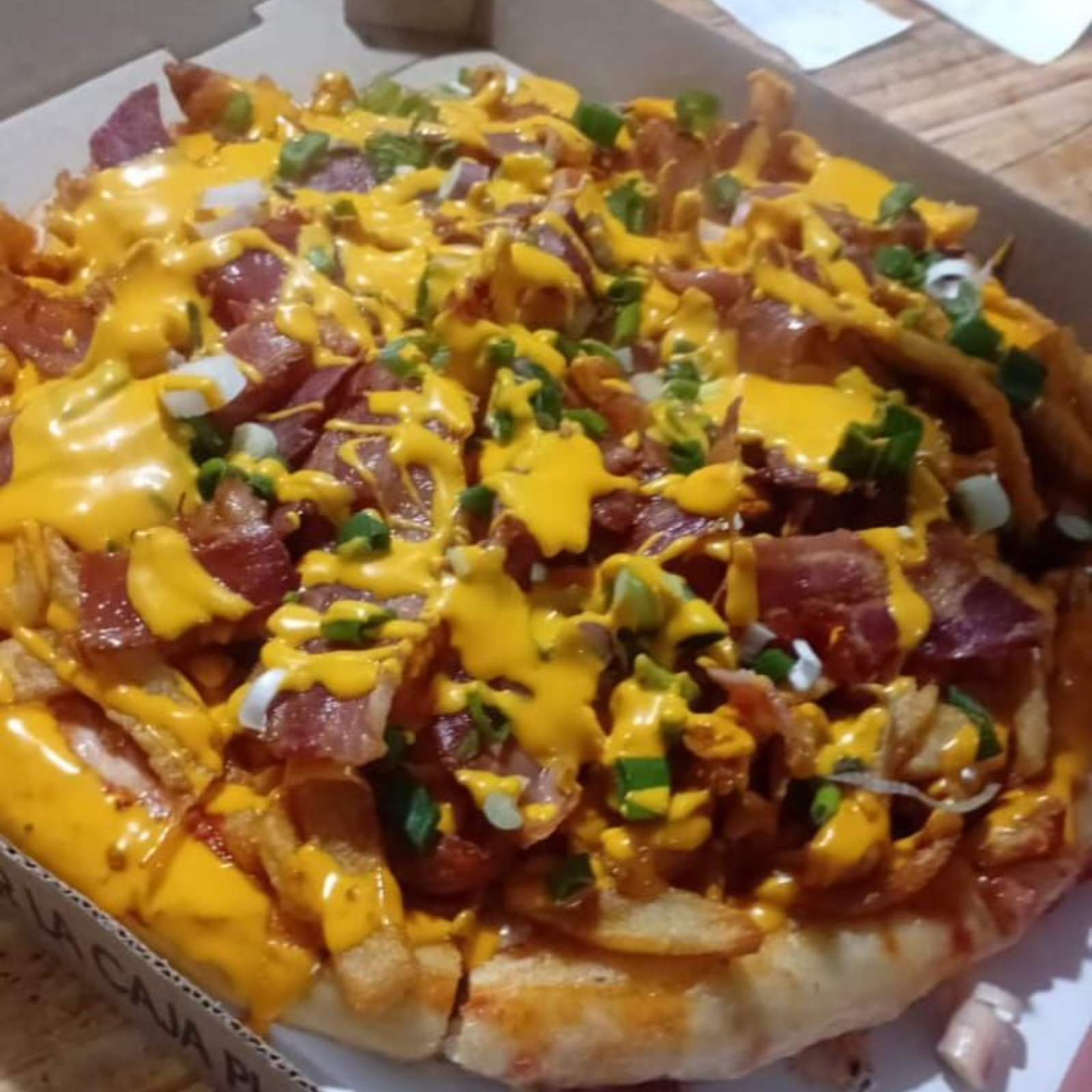 Pizza cubierta con papas fritas, tocino, salsa de queso y cebollas verdes.