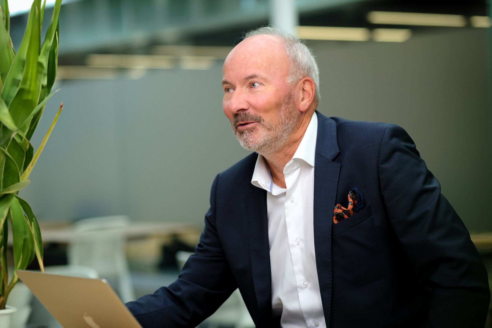 En mann i dress sitter foran en bærbar datamaskin.