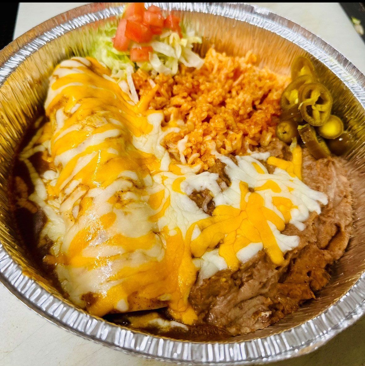 A close up of a foil container filled with mexican food.