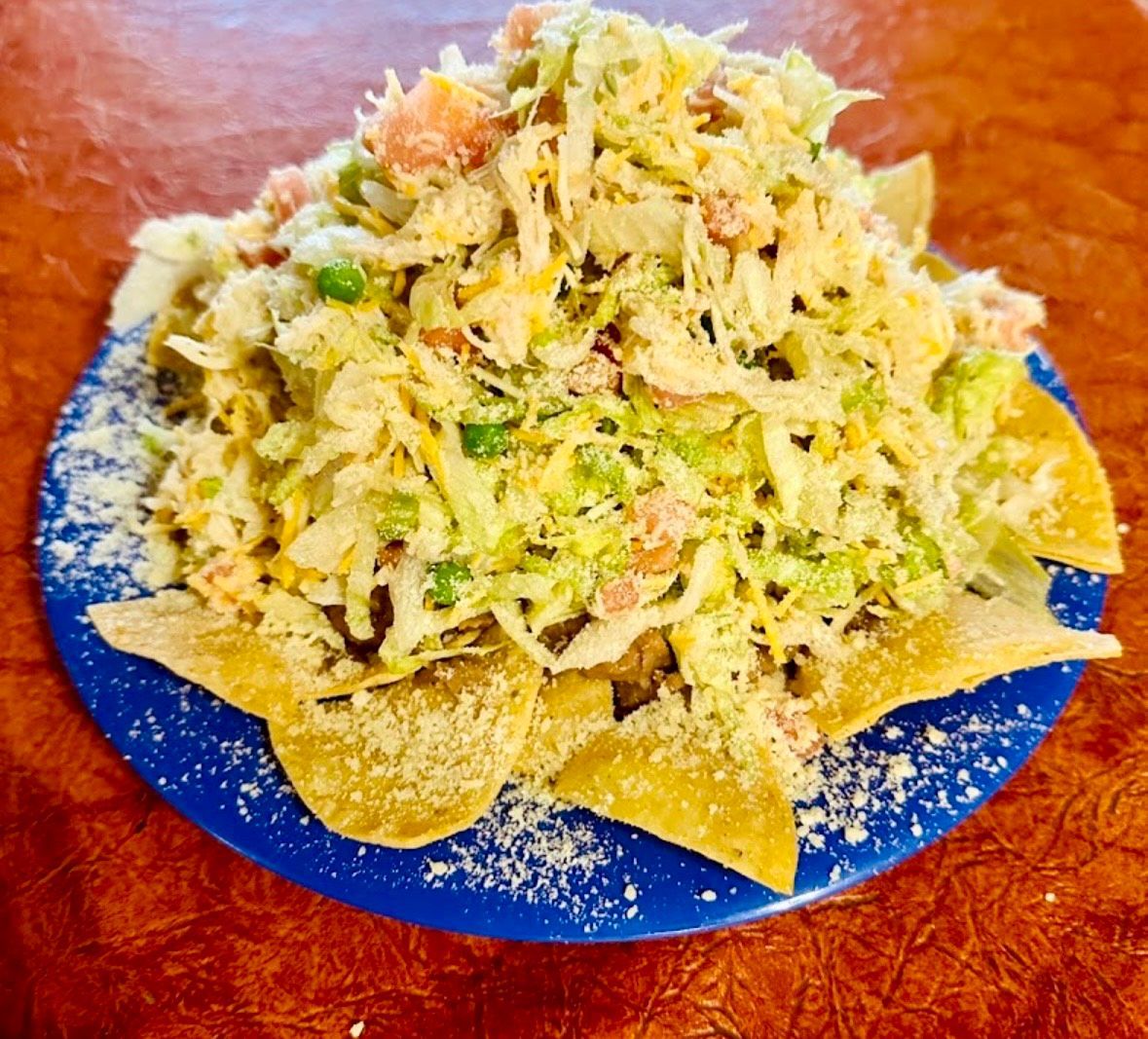 A bowl of tortilla chips with guacamole and cheese on a table.