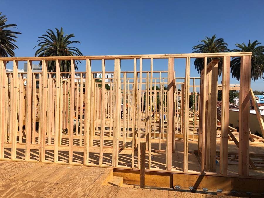 Wooden framework of a building under construction, set against a blue sky and palm trees.
