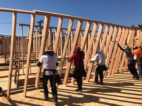 Construction workers lifting wooden wall frame outdoors under a blue sky.