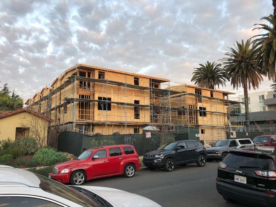 Construction of a multi-story building; wooden frames with scaffolding on a street lined with cars.