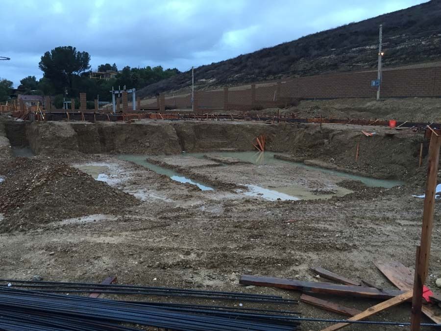 Construction site with excavated foundation, muddy ground, and retaining wall.